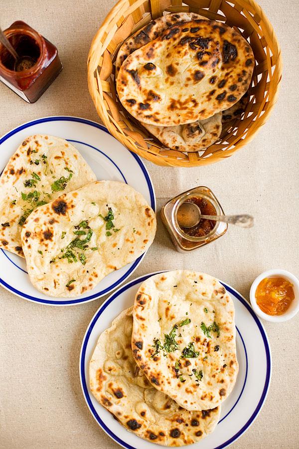 A rustic wooden table set with a bowl of Malai Kofta, rice, and naan bread.