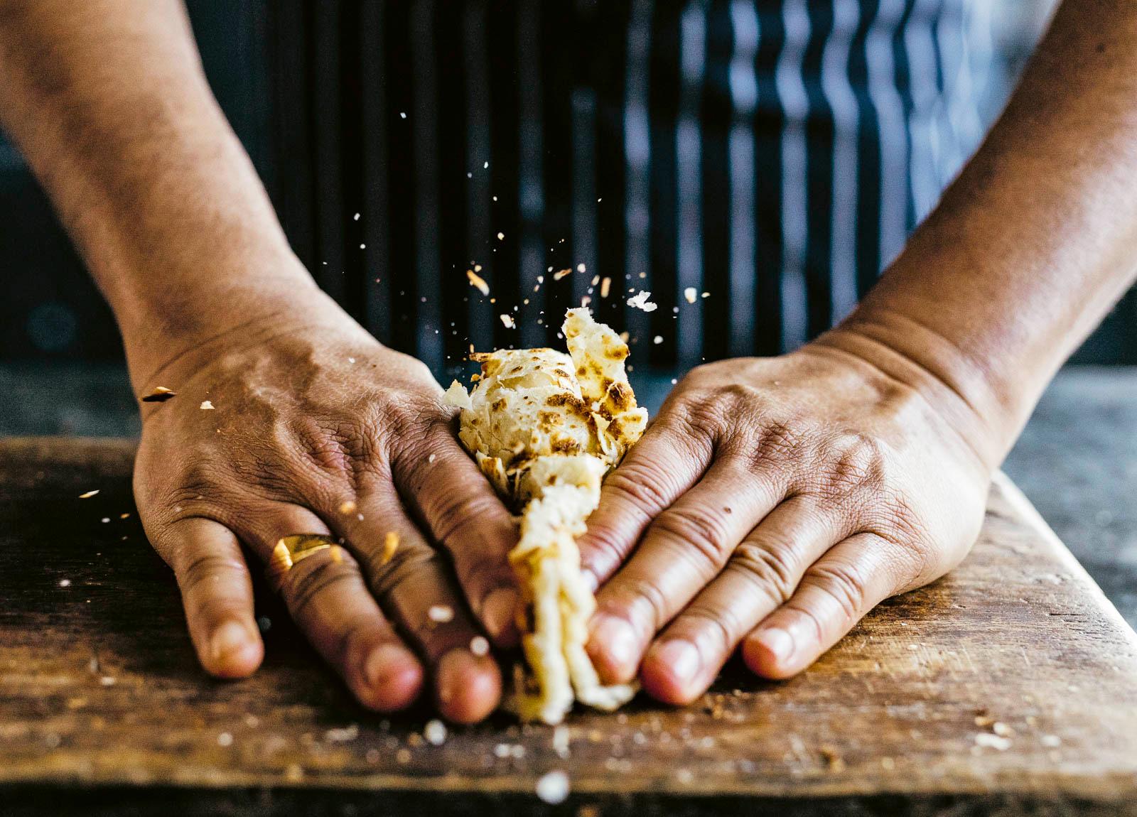 close-up shot of a hand brushing saffron honey ghee onto a warm roti