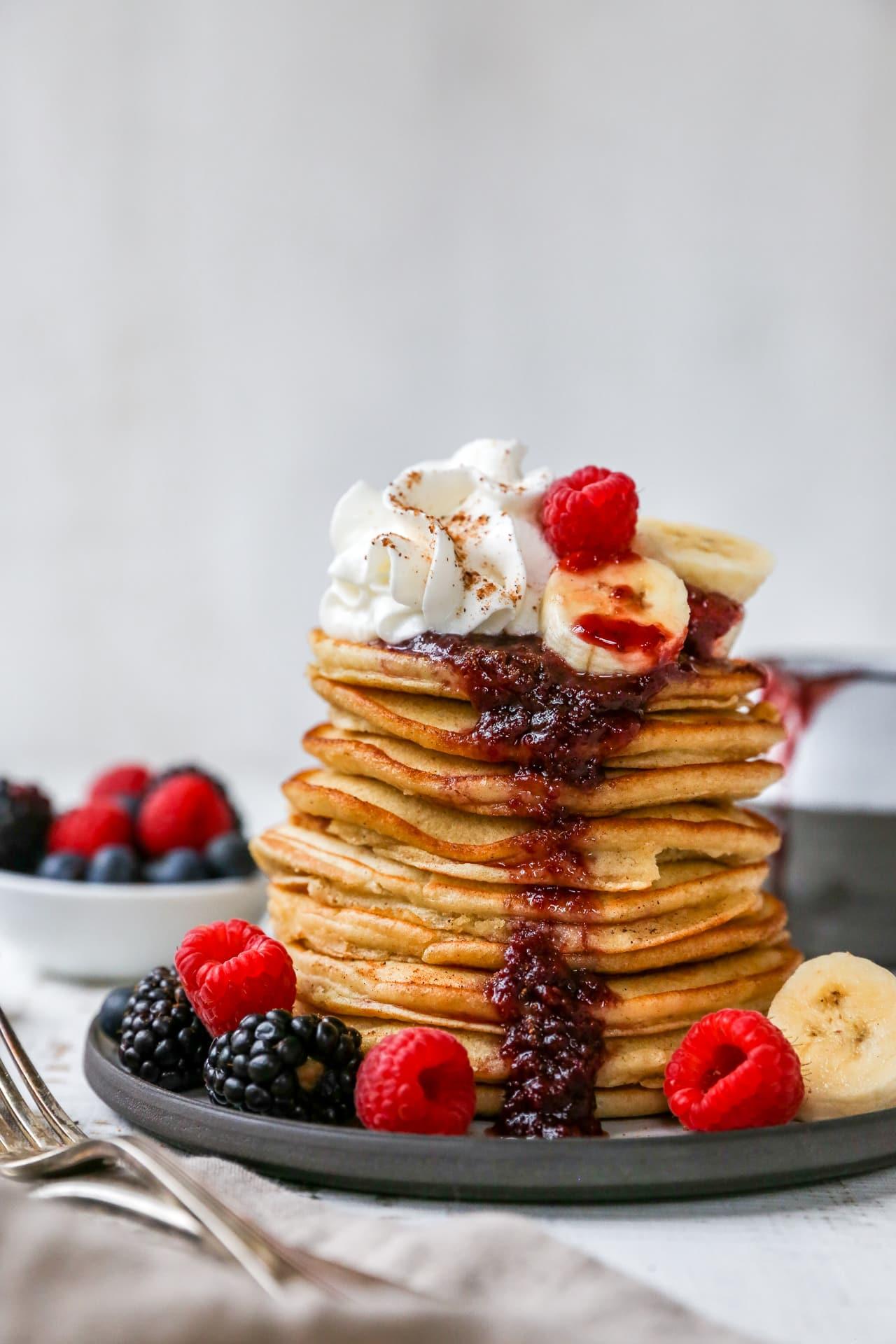A stack of golden-brown banana pancakes topped with whipped cream and fresh berries