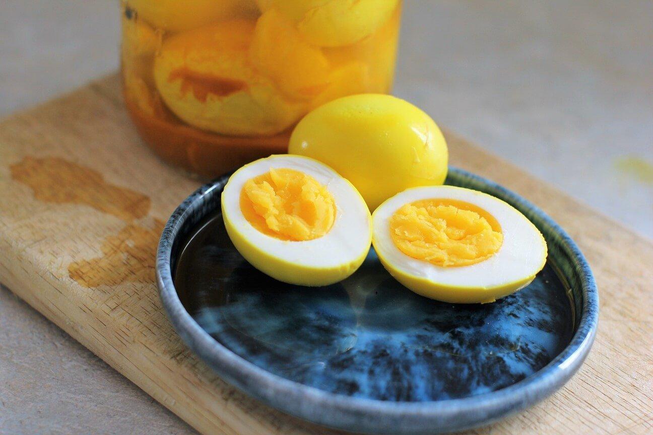 Close-up shot of vibrant golden turmeric boiled eggs in a bowl, garnished with fresh herbs