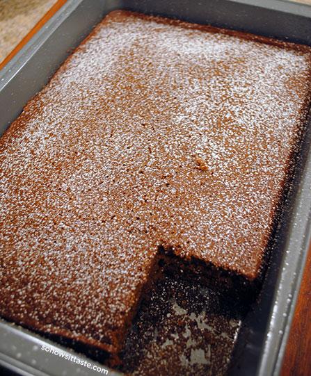 A rustic wooden table with a 9x13 inch baking pan filled with freshly baked gingerbread, garnished with powdered sugar