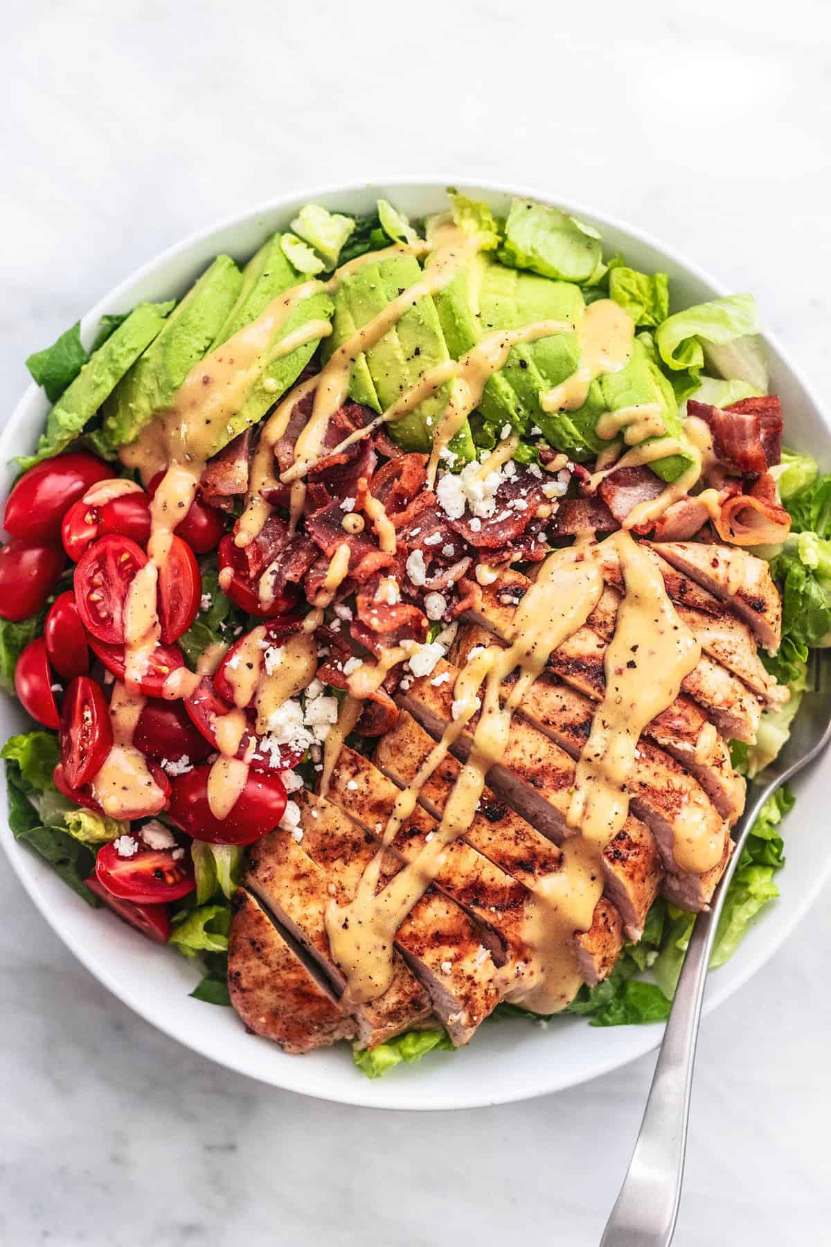 A platter of grilled chicken with avocado ranch, served with a side salad.