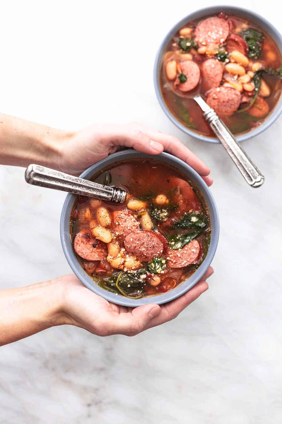 A close-up shot of a spoonful of sausage and bean soup being lifted from a bowl