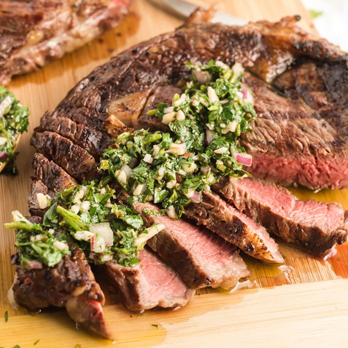 Close-up shot of a grilled ribeye steak with chimichurri sauce drizzled over it.