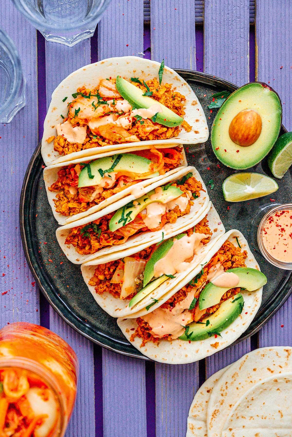 A person happily assembling kimchi orange salad tacos