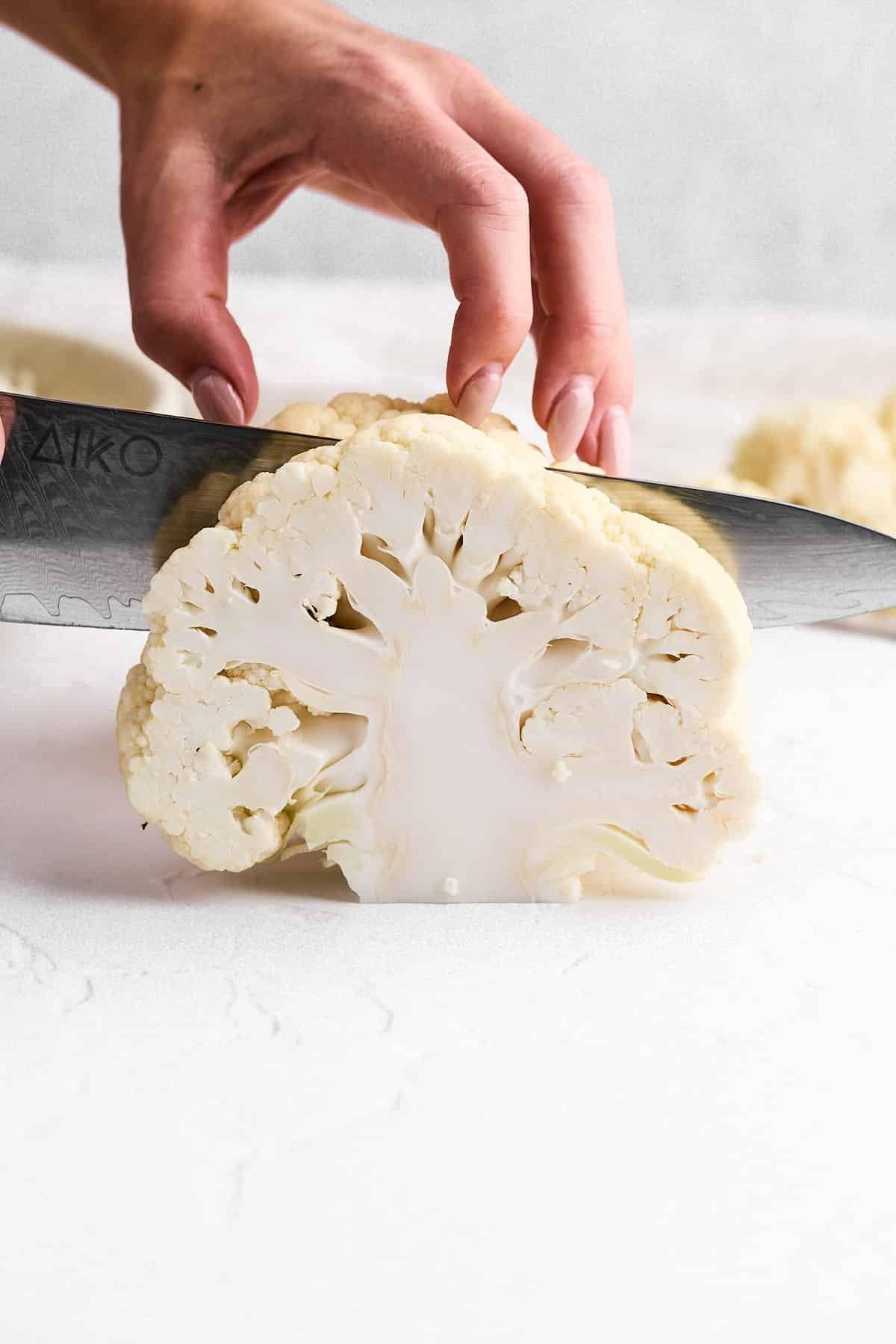 raw cauliflower head being cut into steaks