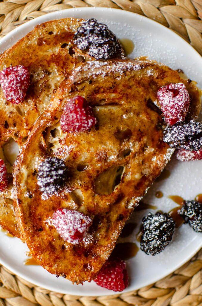 Close up shot of a slice of French toast drizzled with syrup and topped with fruit