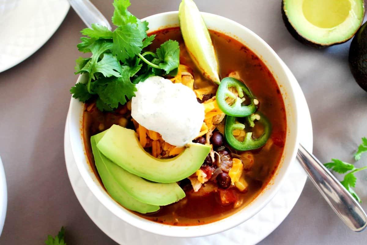 A steaming bowl of Chicken Tortilla Soup garnished with sour cream, avocado, and cilantro