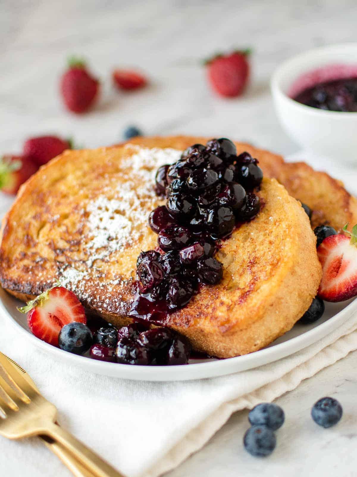 golden brown slices of french toast with a dollop of sour cream and berries on a plate