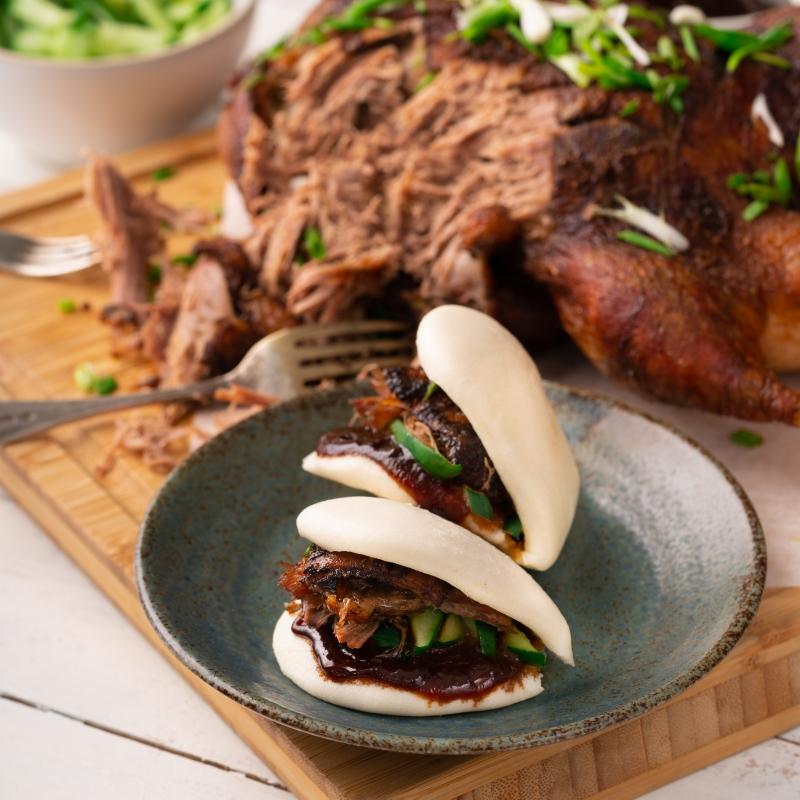 Close-up shot of a delicious Chinese Five-Spice Duck Sandwich on a rustic wooden board, garnished with fresh herbs