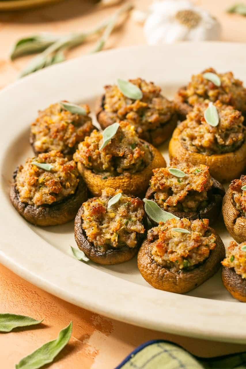 Close-up of golden brown sausage stuffed mushrooms with fresh herbs on a platter