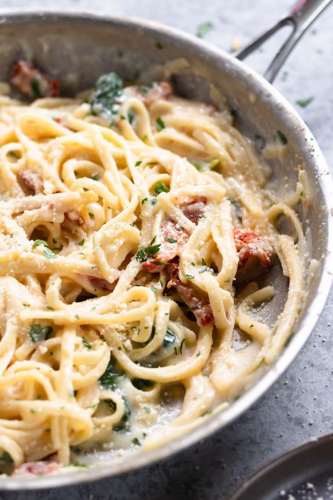 A person enjoying a plate of Chicken Alfredo with sun-dried tomatoes
