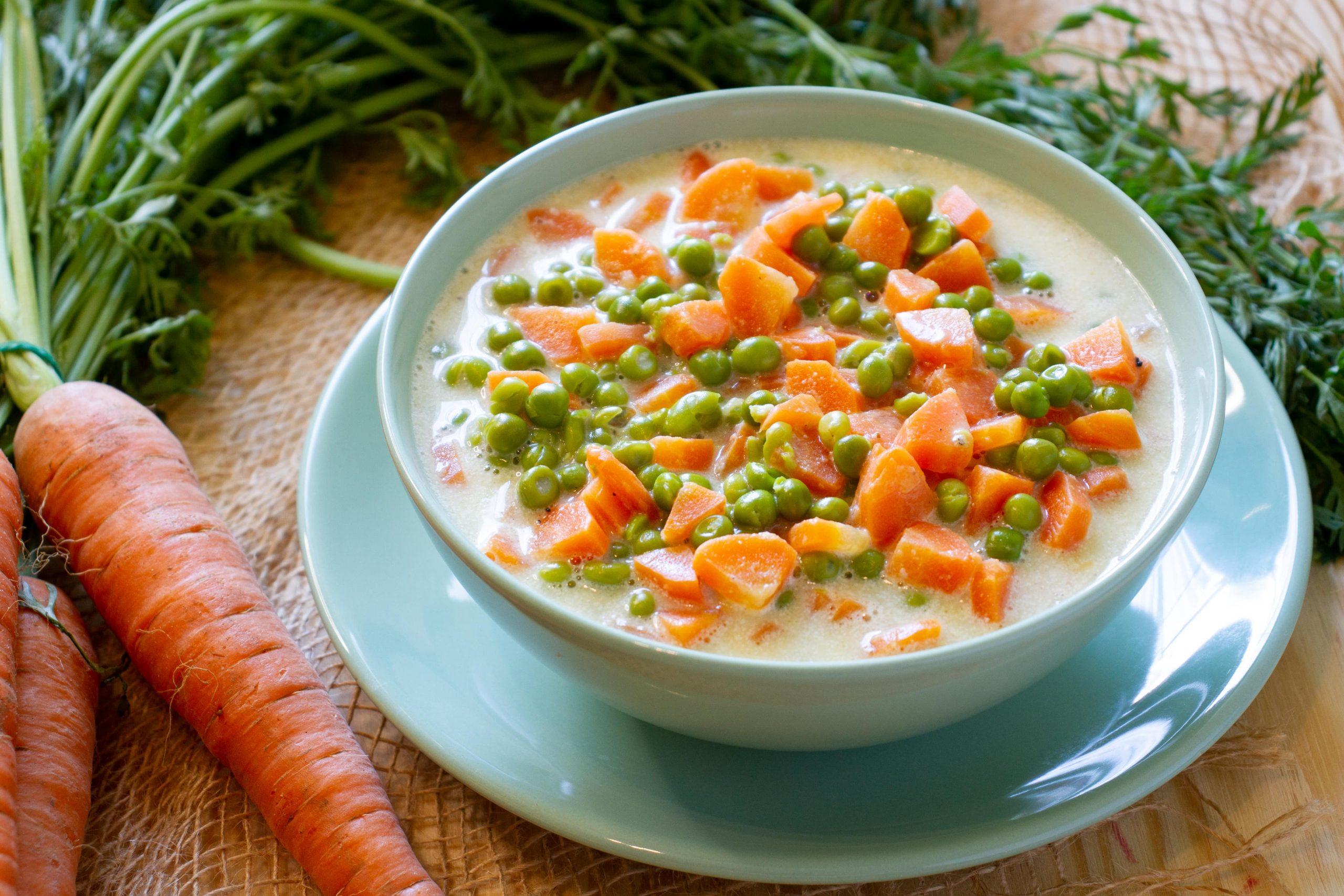 A vibrant close-up shot of sautéed peas and carrots with a dollop of crème fraîche, garnished with fresh parsley.