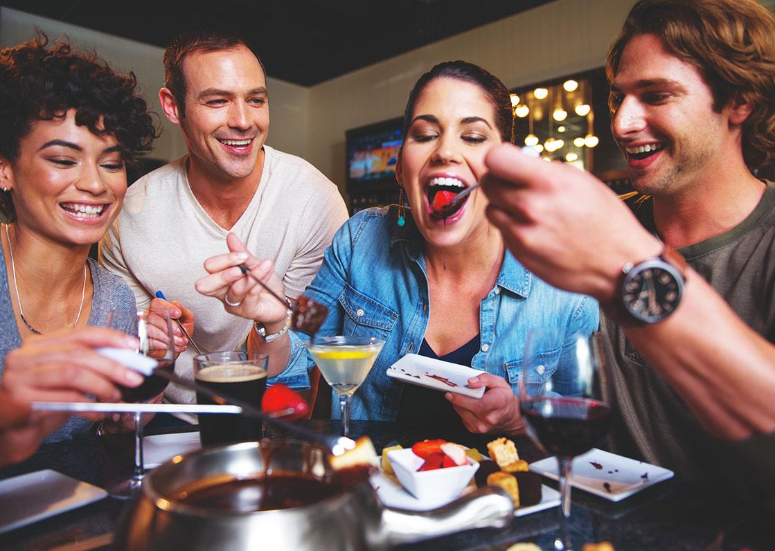 A group of people gathered around a chocolate fondue pot, laughing and enjoying themselves