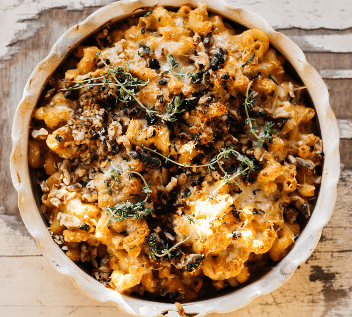 A serving of mac and cheese with walnuts, garnished with fresh herbs
