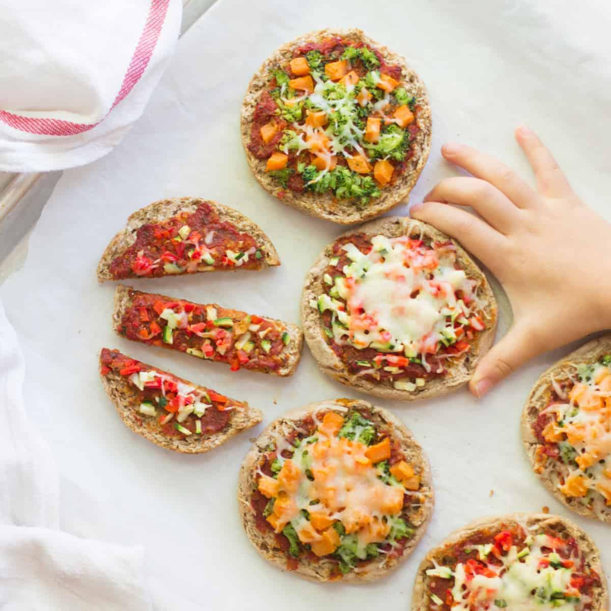 A child happily adding toppings to a mini pizza on an English muffin