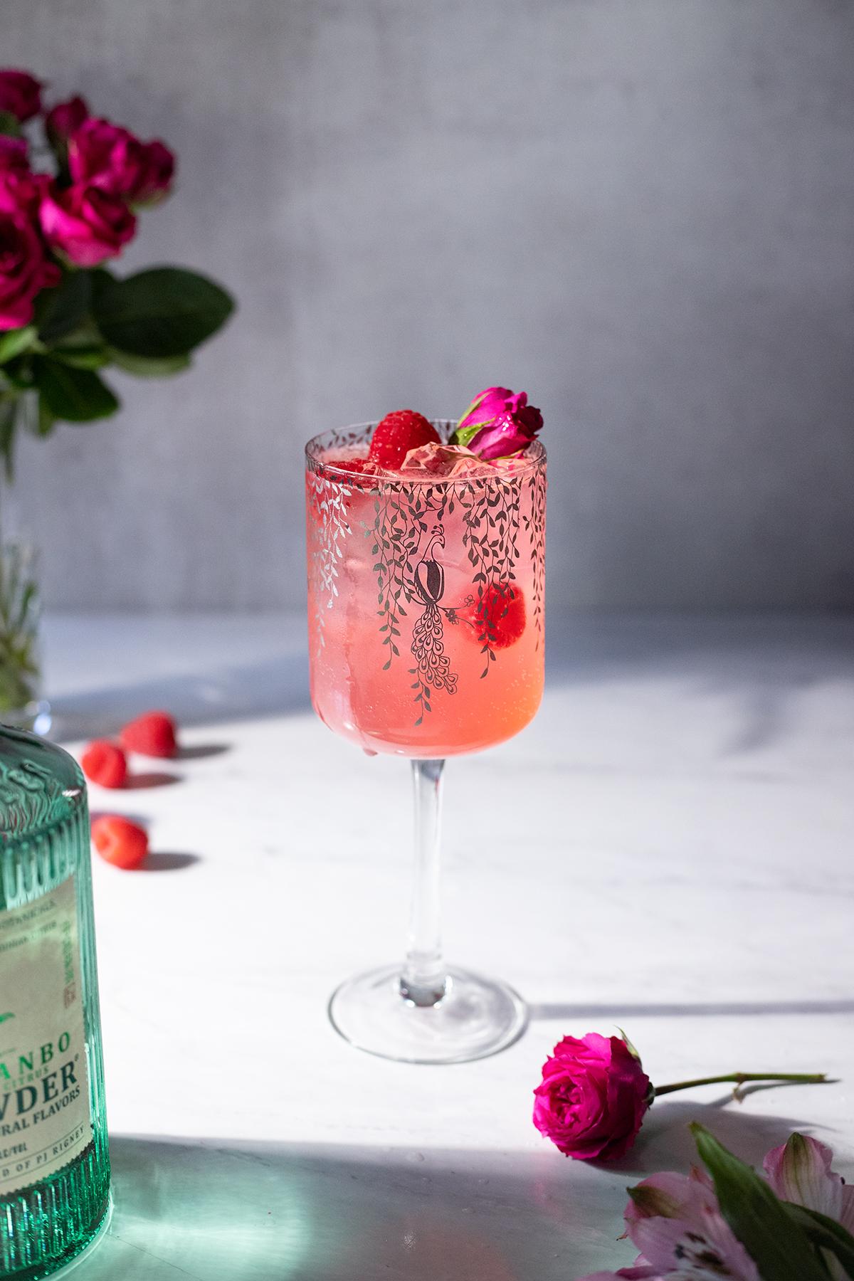 Close-up shot of a vibrant pink Raspberry Rose Smoothie in a glass with fresh raspberries and rose petals garnishing it.