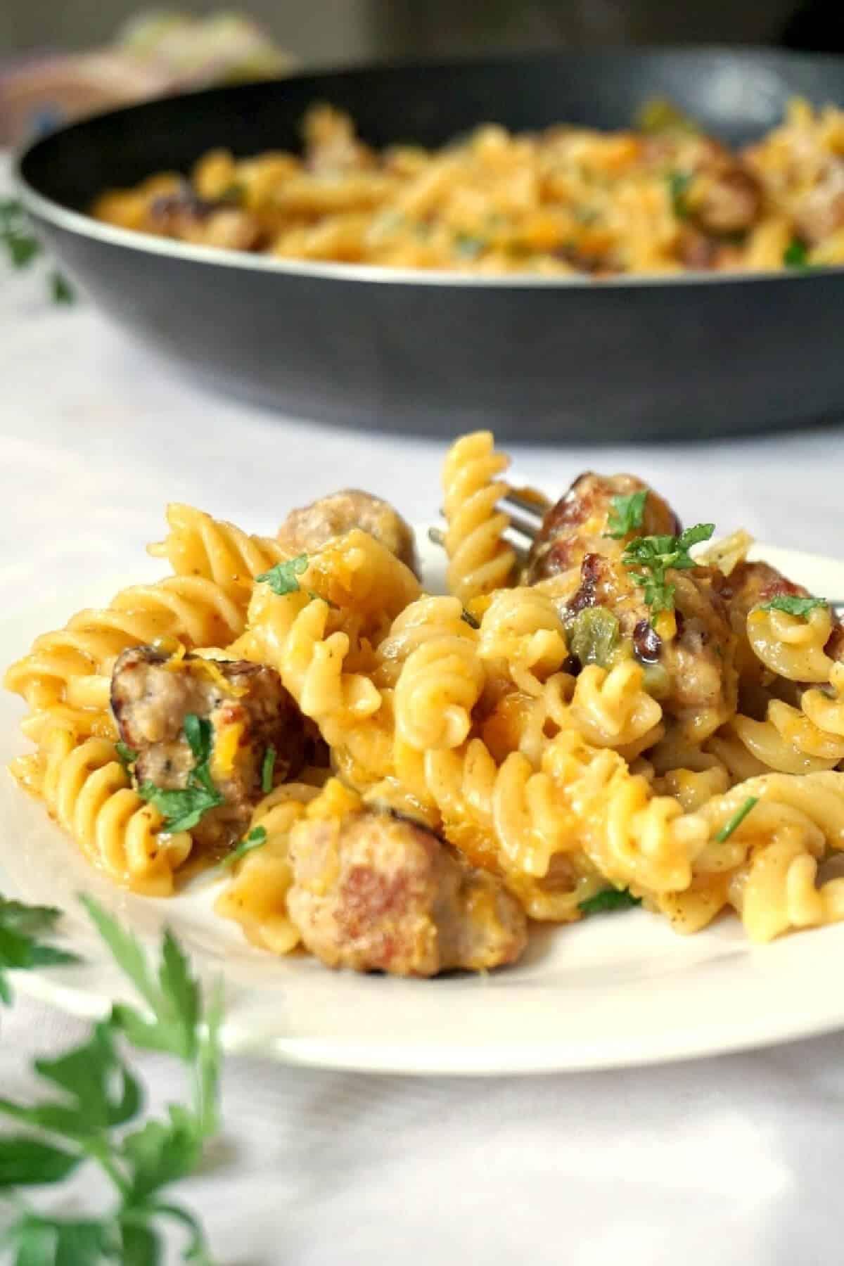 A person enjoying a plate of butternut squash and sausage pasta