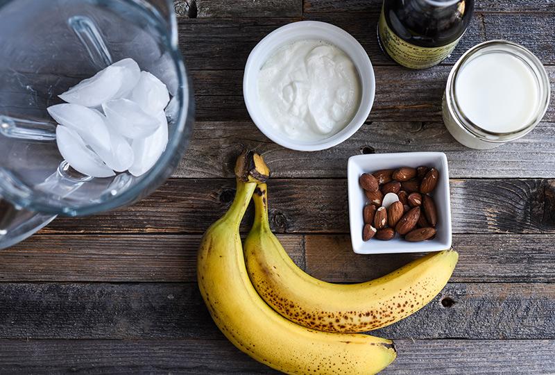 A variety of smoothie ingredients such as bananas, almonds, and vanilla bean arranged artistically