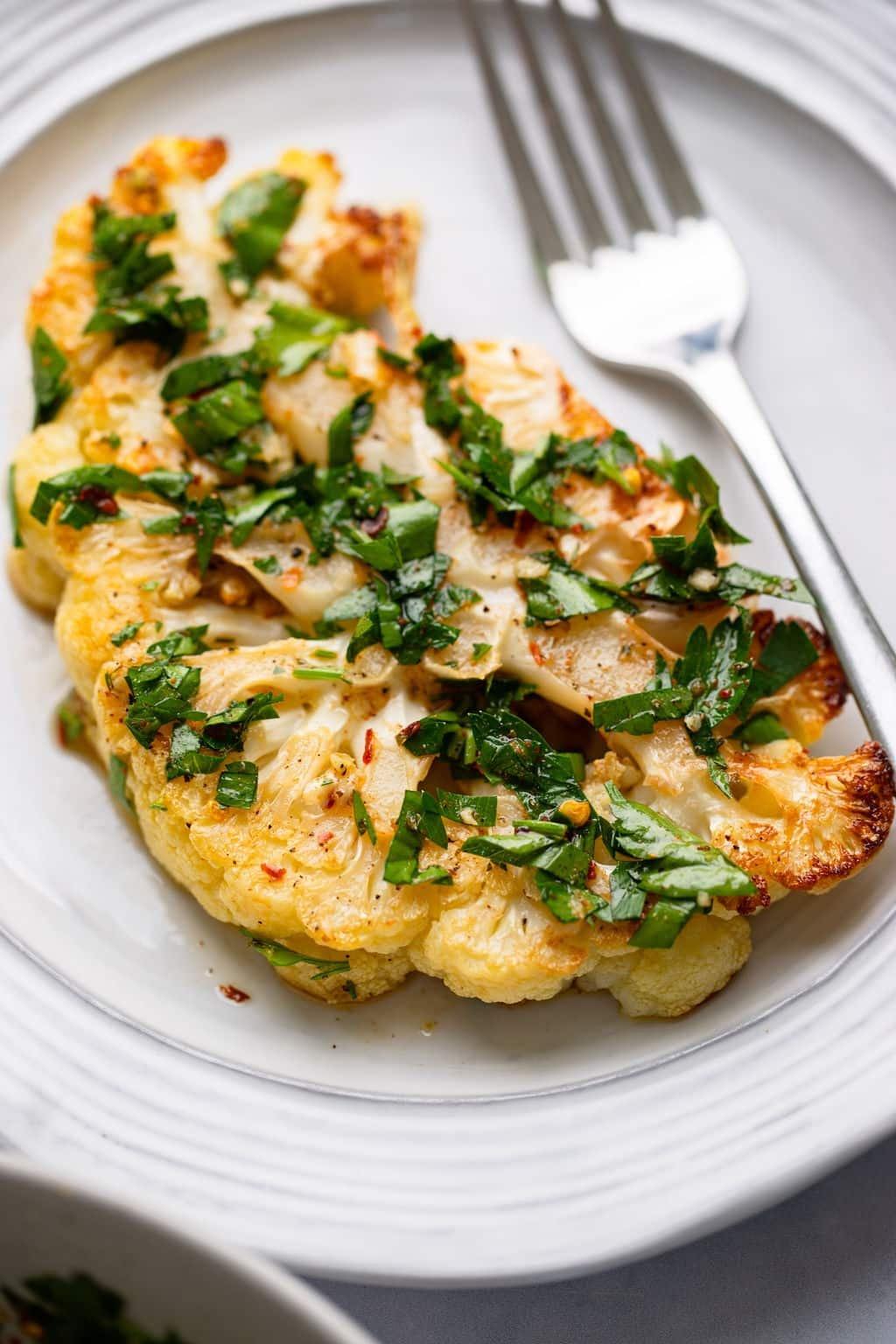 Various herbs and spices arranged around a plate of cauliflower steaks.