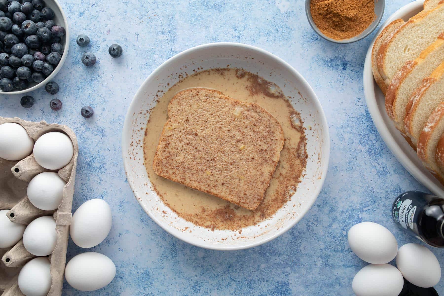 Close-up shot of a person dipping bread into a bowl of custard mixture