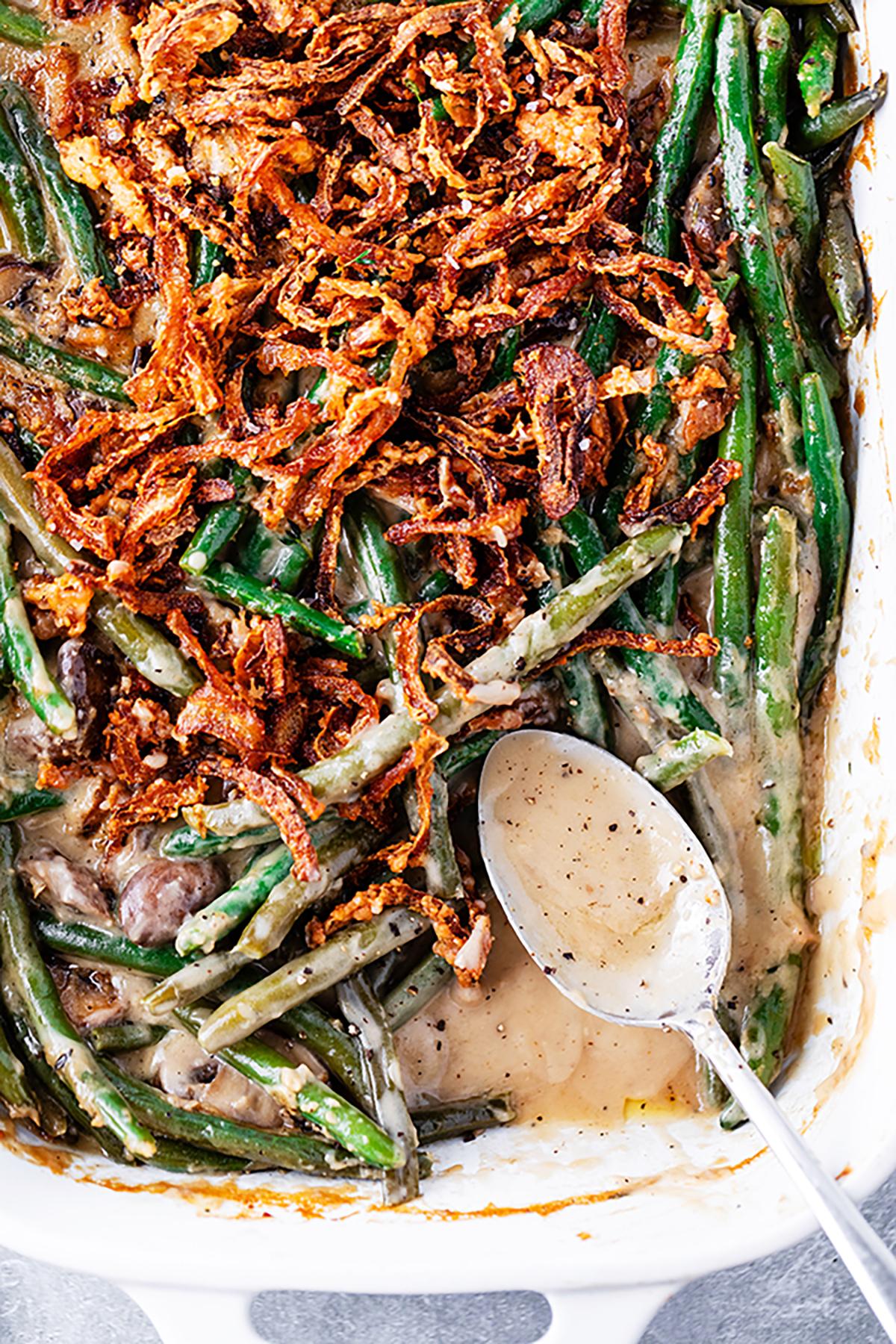 Homemade green bean casserole with golden crispy fried onions on top, close up, warm lighting, rustic table setting, shallow depth of field.
