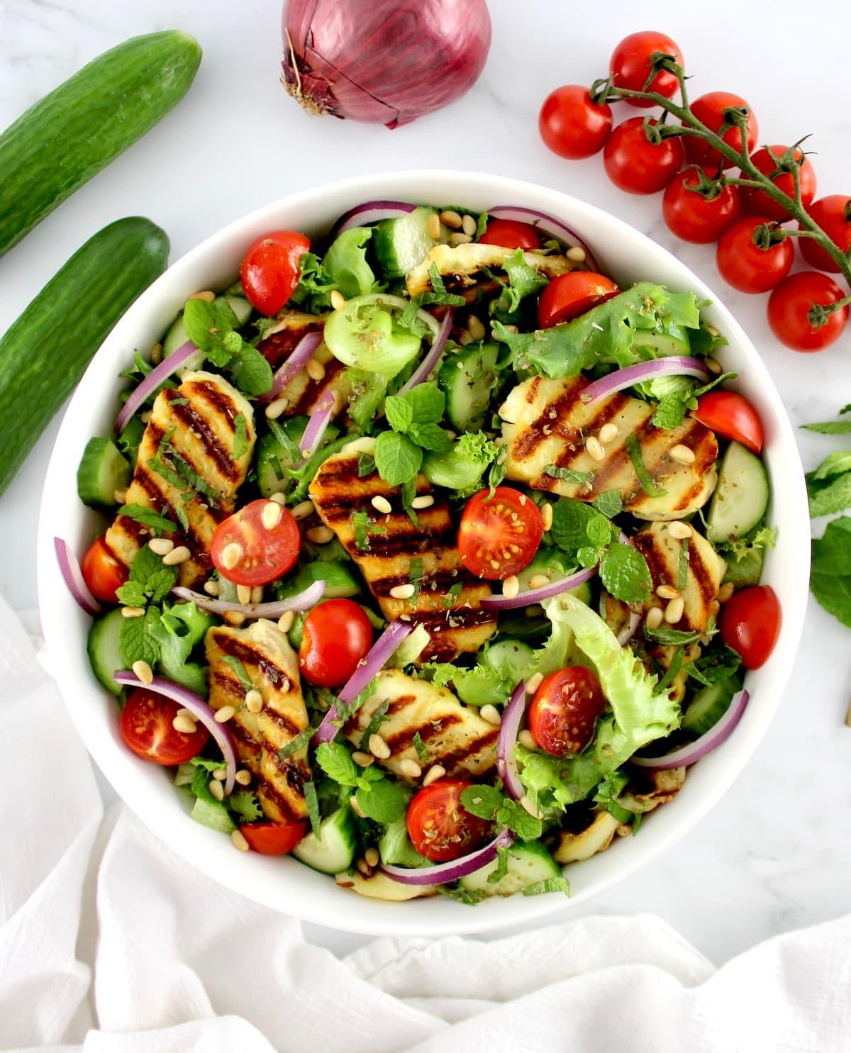overhead view of a large bowl of grilled halloumi salad being served
