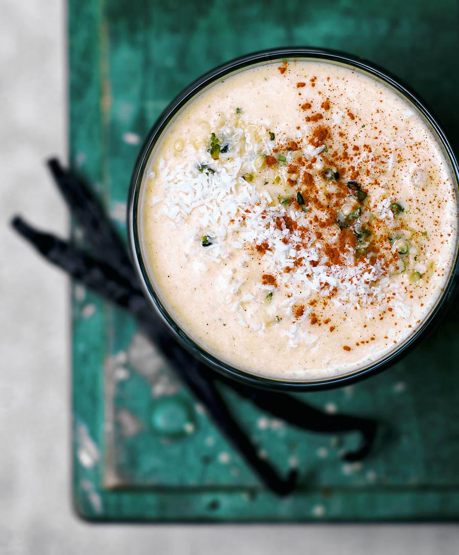 A close-up shot of a vibrant orange Kabocha Squash and Coconut Milk Smoothie in a clear glass, garnished with a sprinkle of cinnamon and a sprig of mint