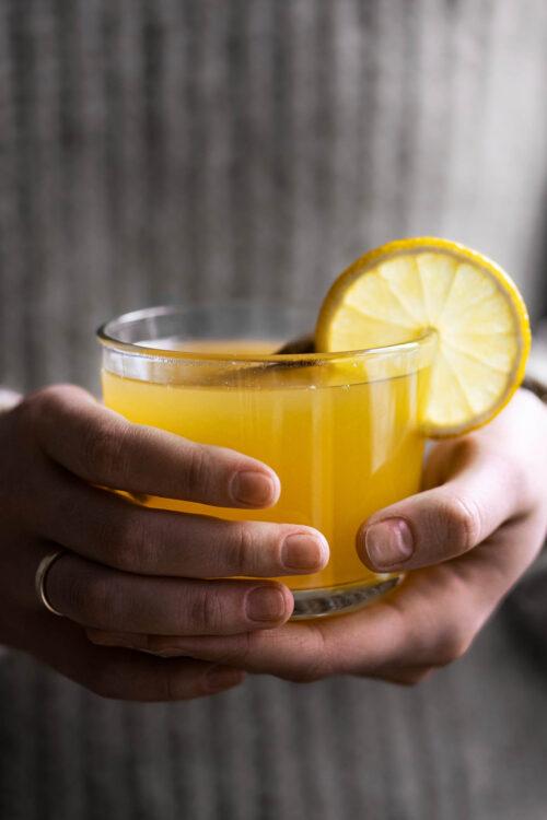 Person enjoying a glass of Ginger Lemon Turmeric Lemonade outdoors in a scenic setting