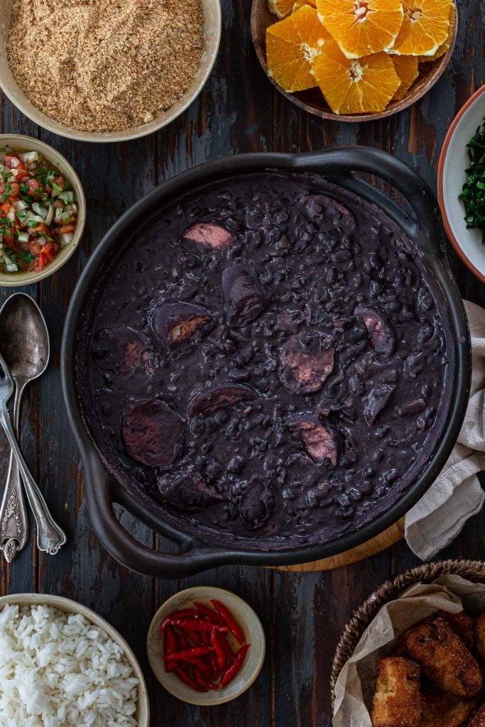 A steaming pot of feijoada with crispy fried plantains on the side