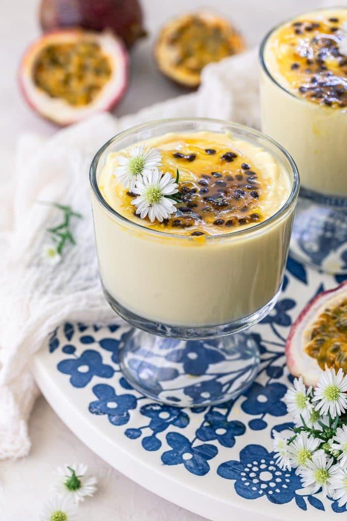 Close-up shot of a silky smooth passion fruit mousse in individual glasses, garnished with passion fruit seeds and mint sprigs.