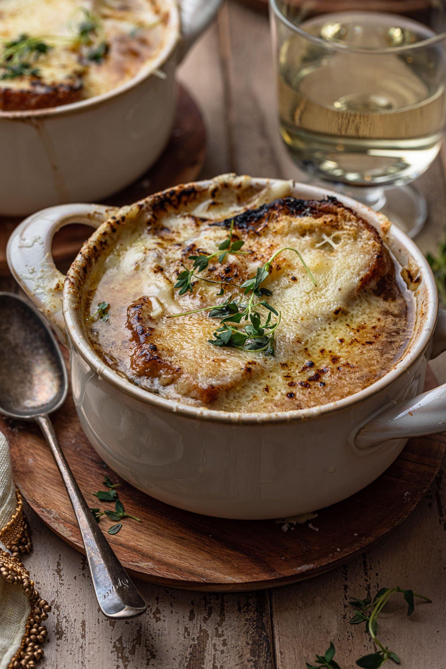 A rustic bowl of creamy cashew cheese French onion soup, garnished with caramelized onions and crusty bread