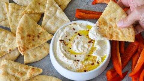 Close-up of a person dipping pita bread into the creamy feta dip