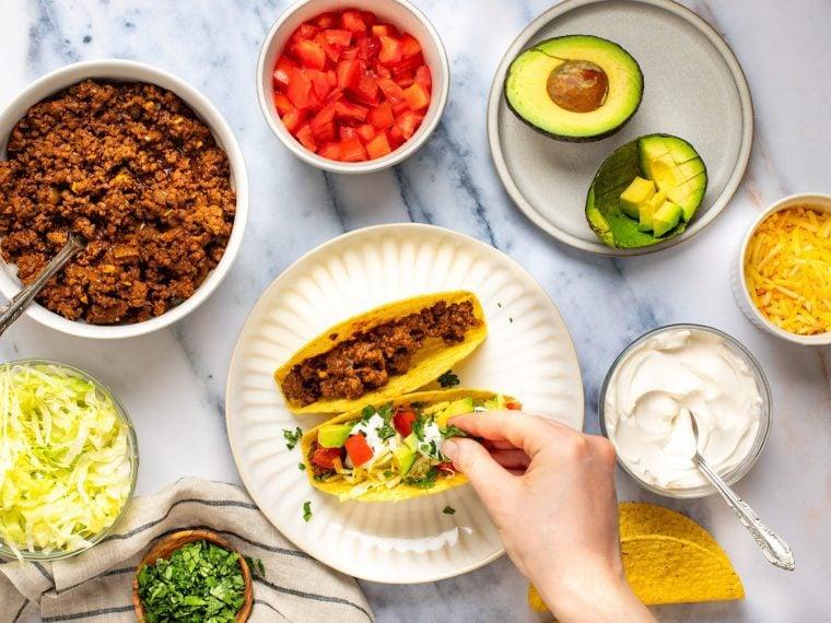 a person assembling beef tacos with various toppings