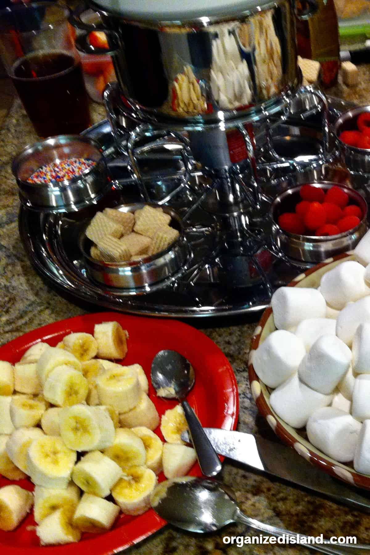 An array of fresh fruits and other treats arranged attractively around a fondue pot.
