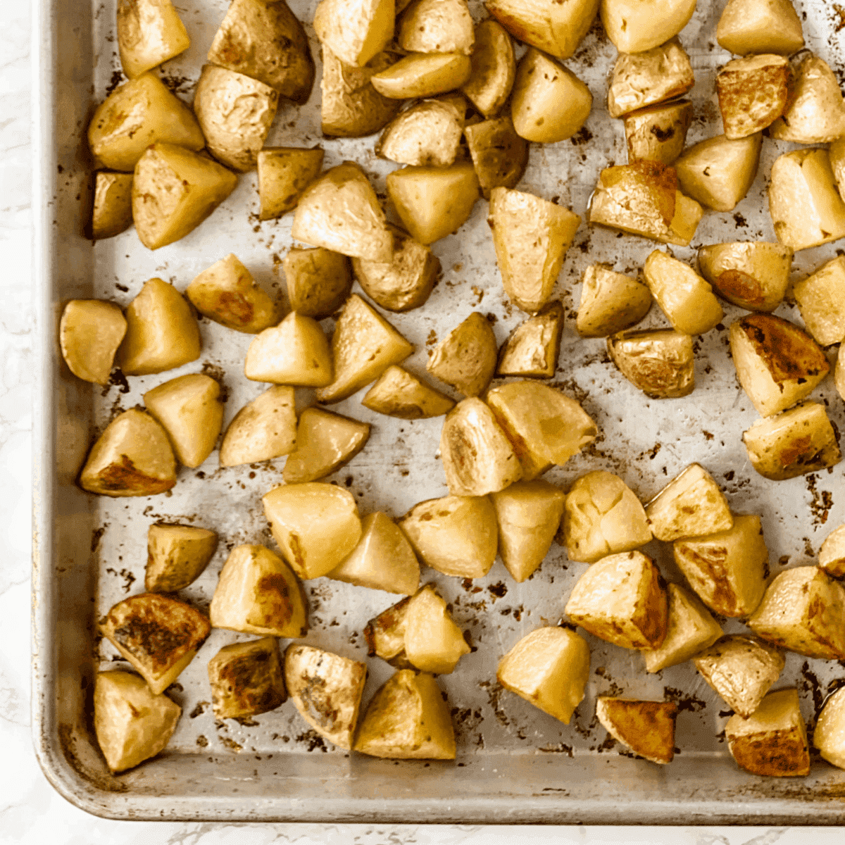 A close up of the potatoes on a baking sheet, halfway through roasting