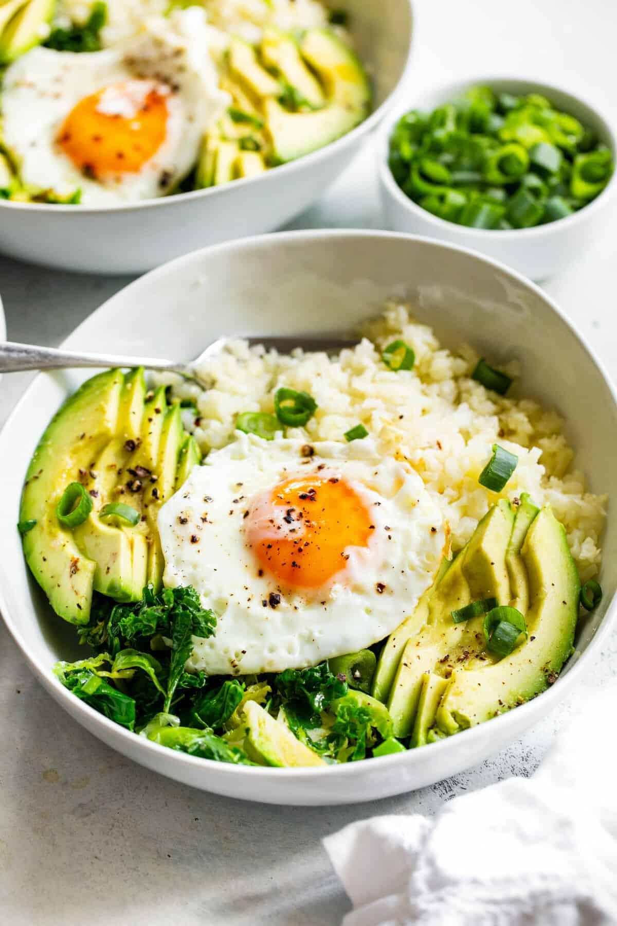 A vibrant and healthy breakfast bowl with cauliflower rice, fried eggs, and avocado.