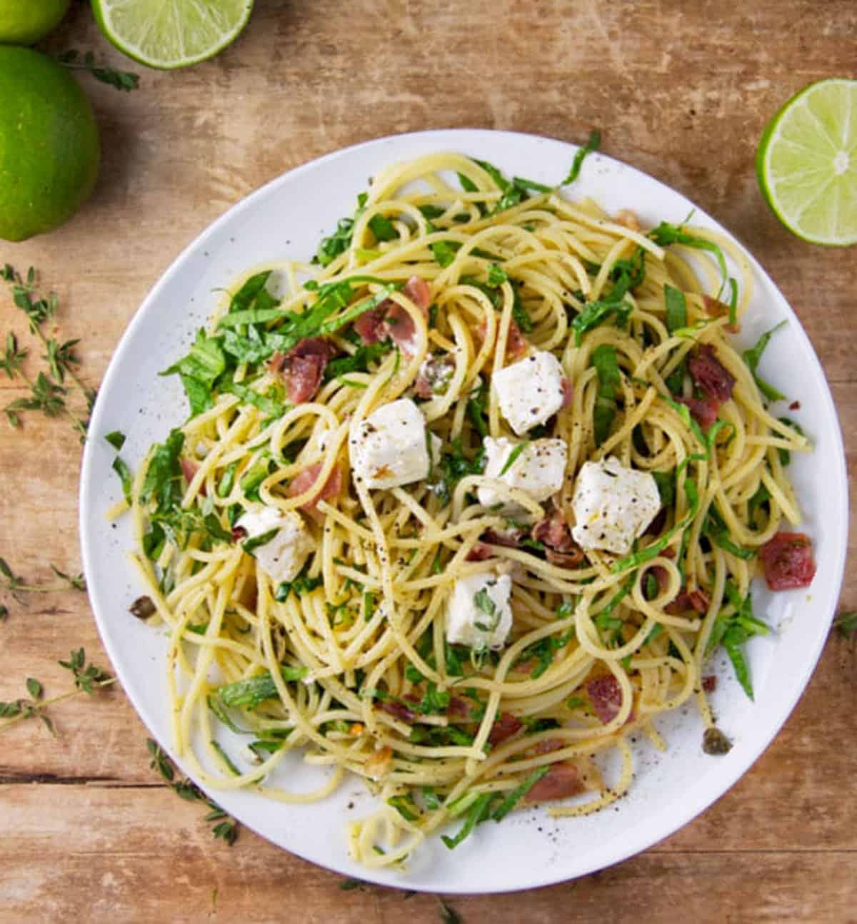 A plate of pasta with prosciutto and arugula, garnished with parmesan cheese
