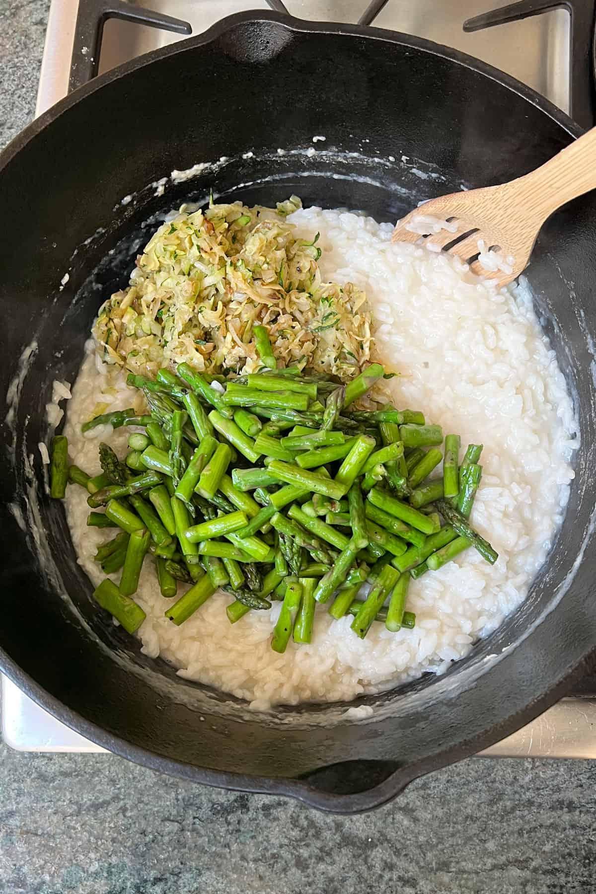 Close-up shot of a person stirring a creamy risotto in a pan, showcasing the vibrant green asparagus and nutty wild rice.