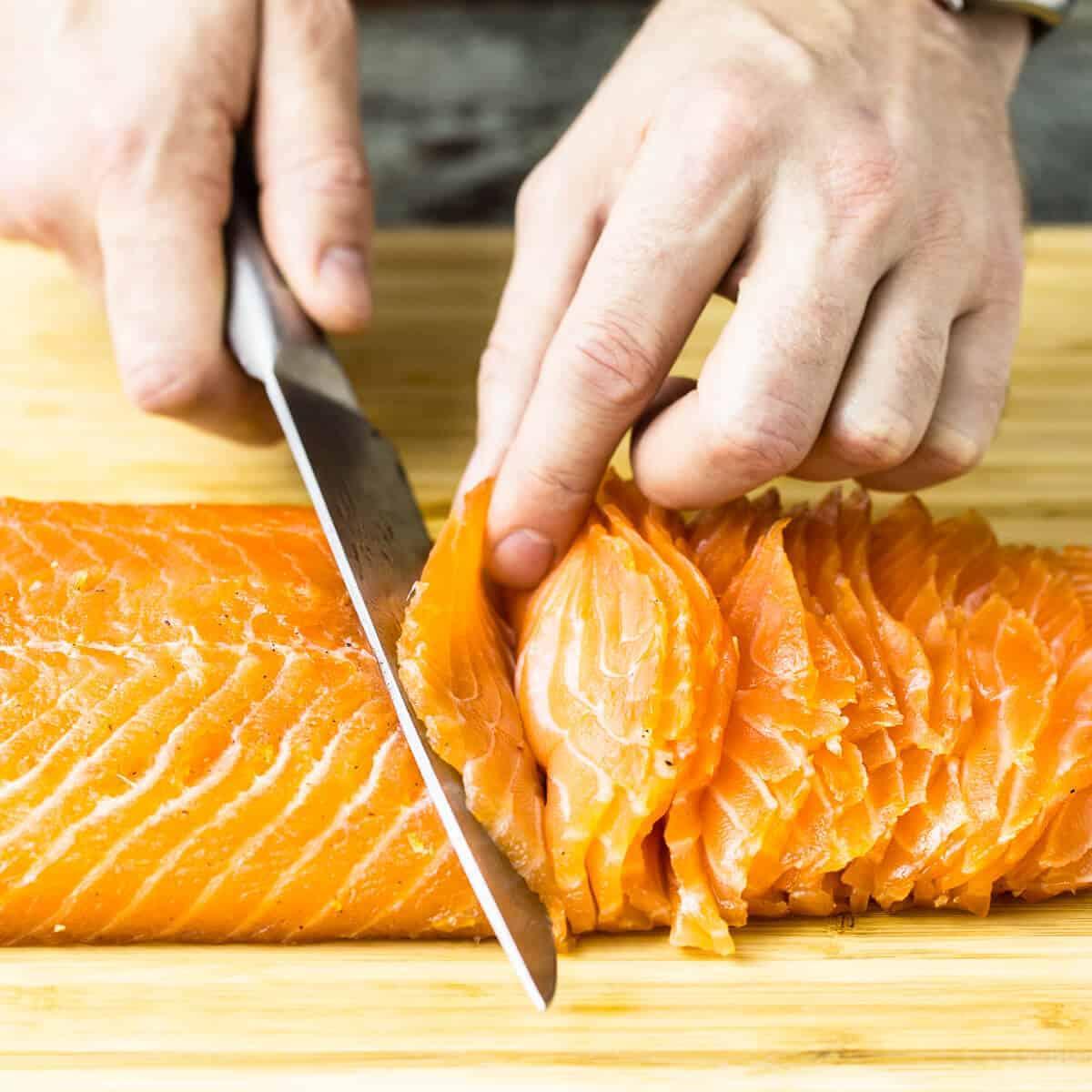 A person carefully slicing gravlax with a sharp knife