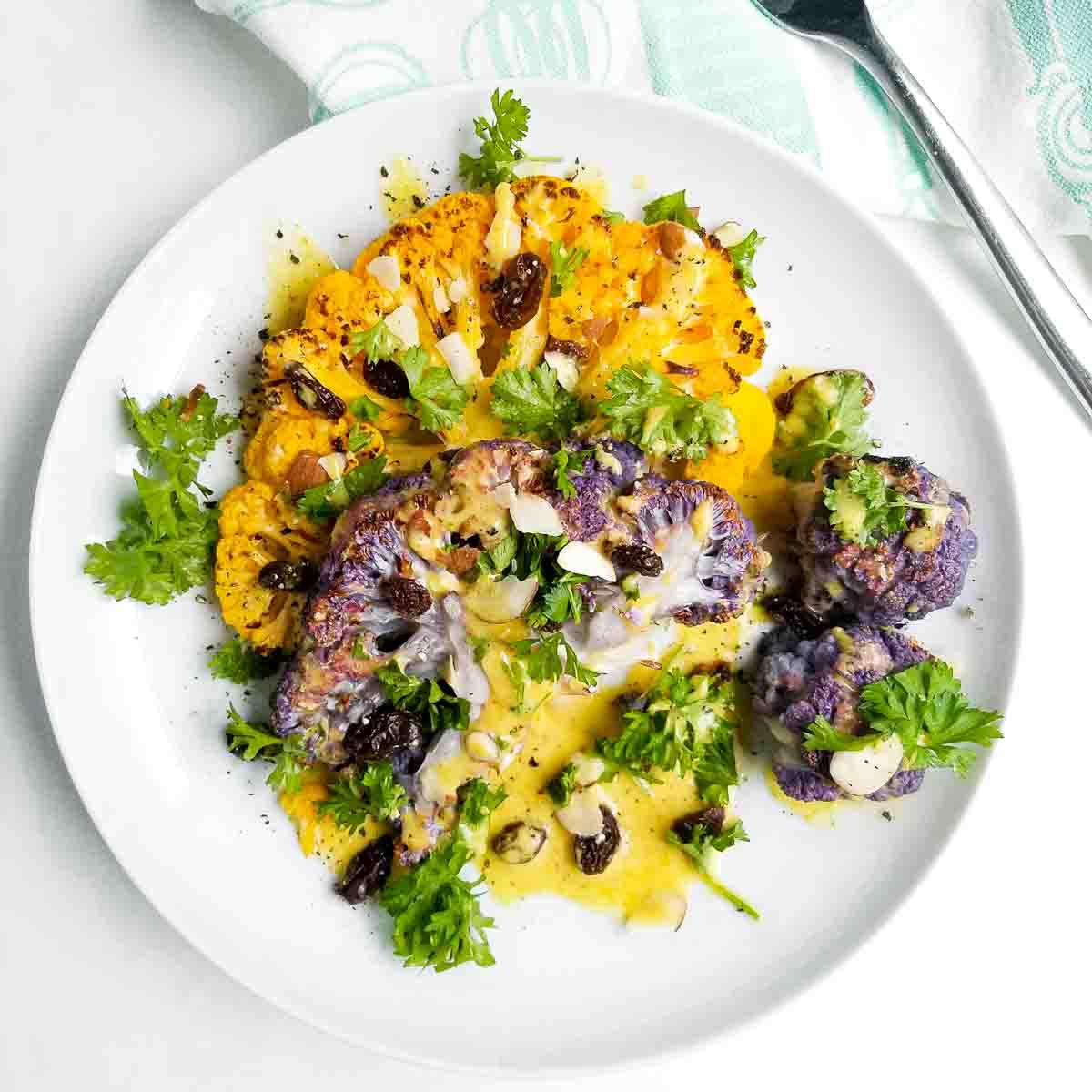 Close-up shot of perfectly seared cauliflower steaks in a coconut curry sauce with assorted colorful vegetables