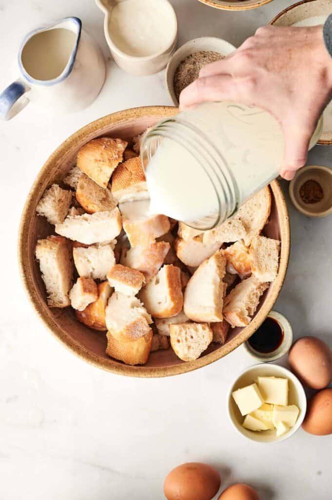 A bowl of ingredients for bread pudding: eggs, milk, sugar, spices, and pieces of stale bread