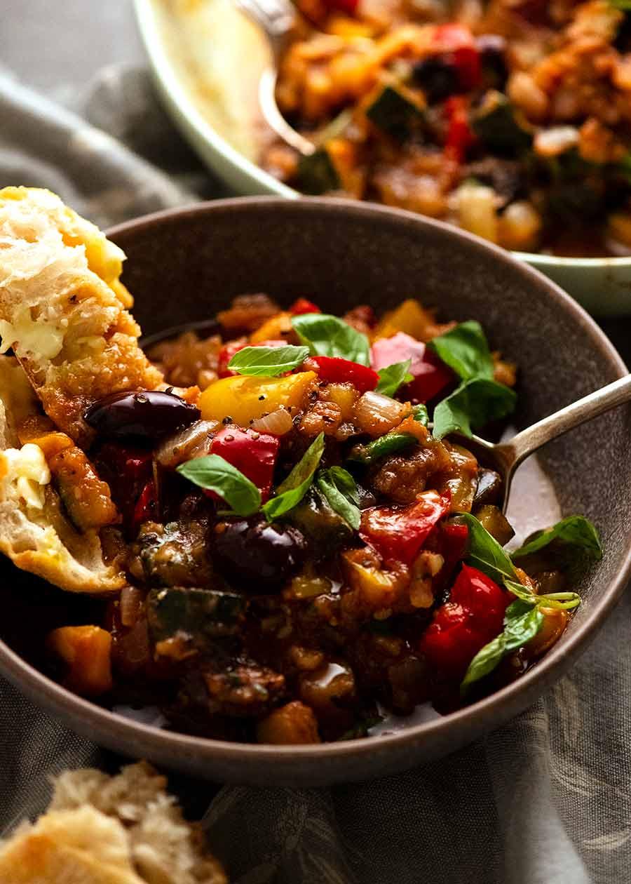 A beautifully presented bowl of Mediterranean vegetable stew, garnished with fresh herbs and crusty bread.
