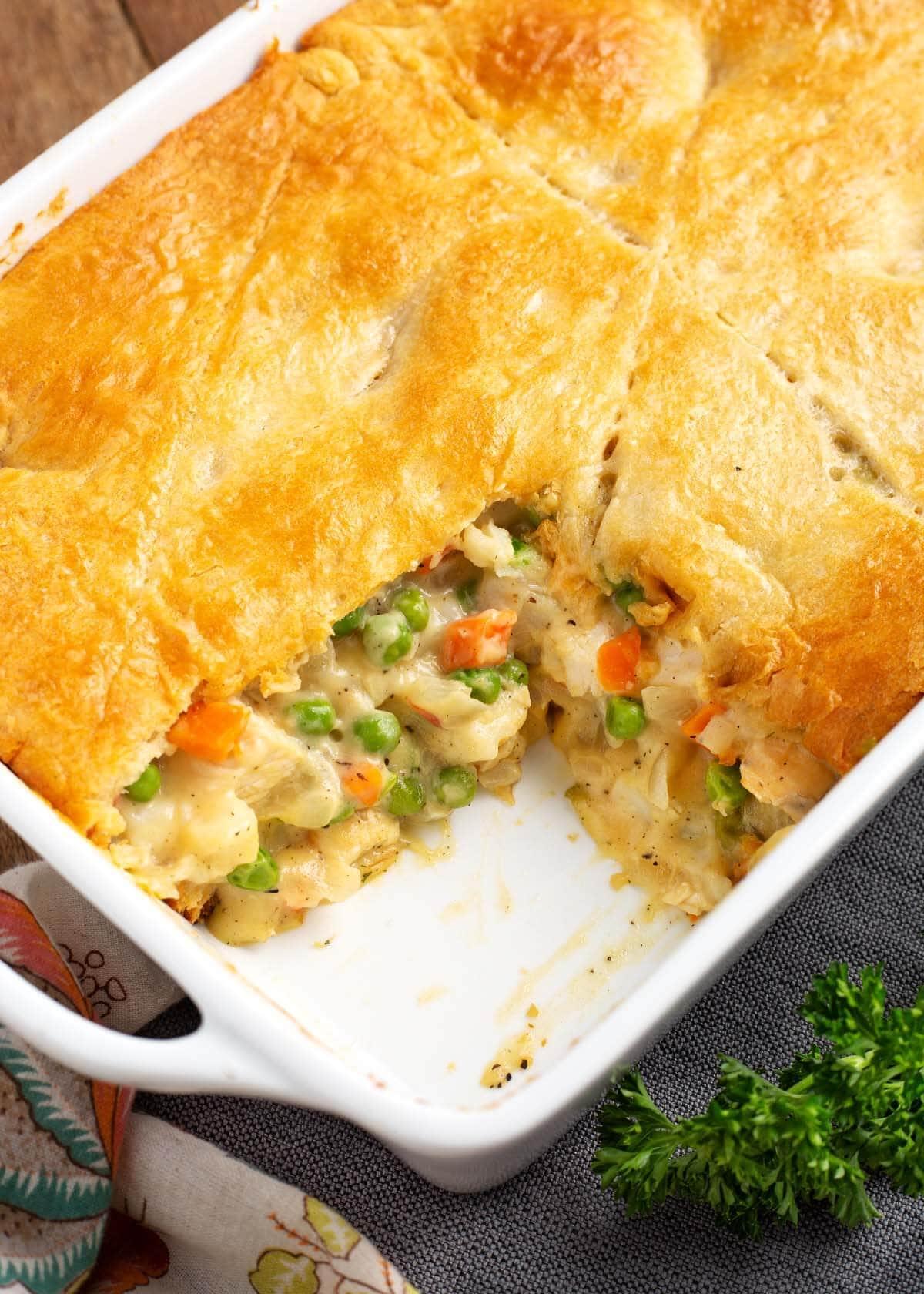 A wider shot showing the entire Chicken Pot Pie Casserole in the baking dish, with a rustic kitchen setting in the background.