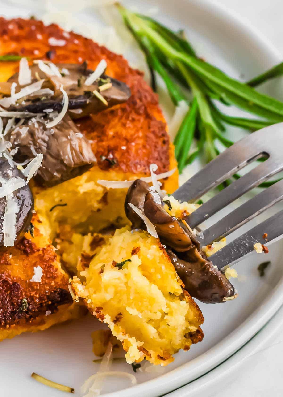 Close-up shot of golden-brown polenta cakes topped with sautéed kale and parmesan cheese, garnished with fresh herbs