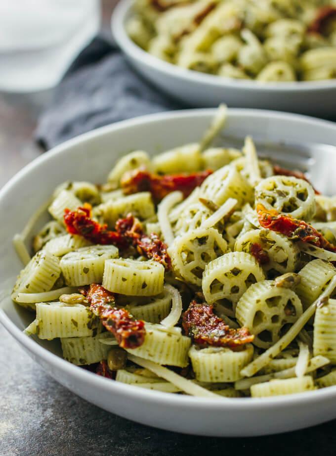 Close-up shot of a bowl of pasta salad with pesto, sun-dried tomatoes, and fresh basil