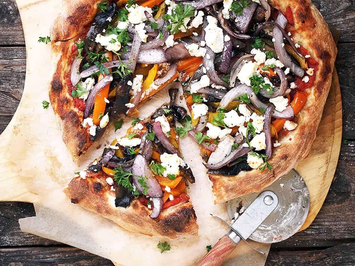 Close up shot of a grilled vegetable pizza with asiago cheese, showcasing the charred vegetables and melted cheese