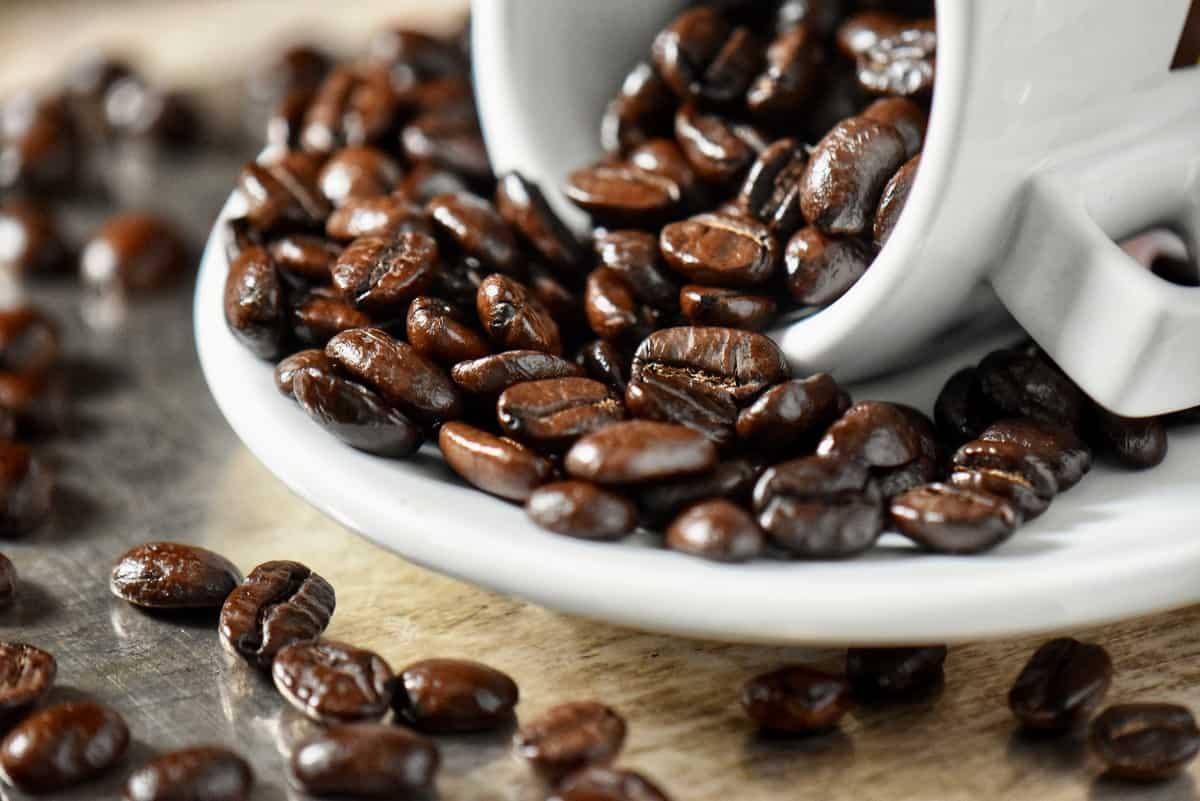 A bowl of chocolate-covered espresso beans, with a cup of coffee in the background