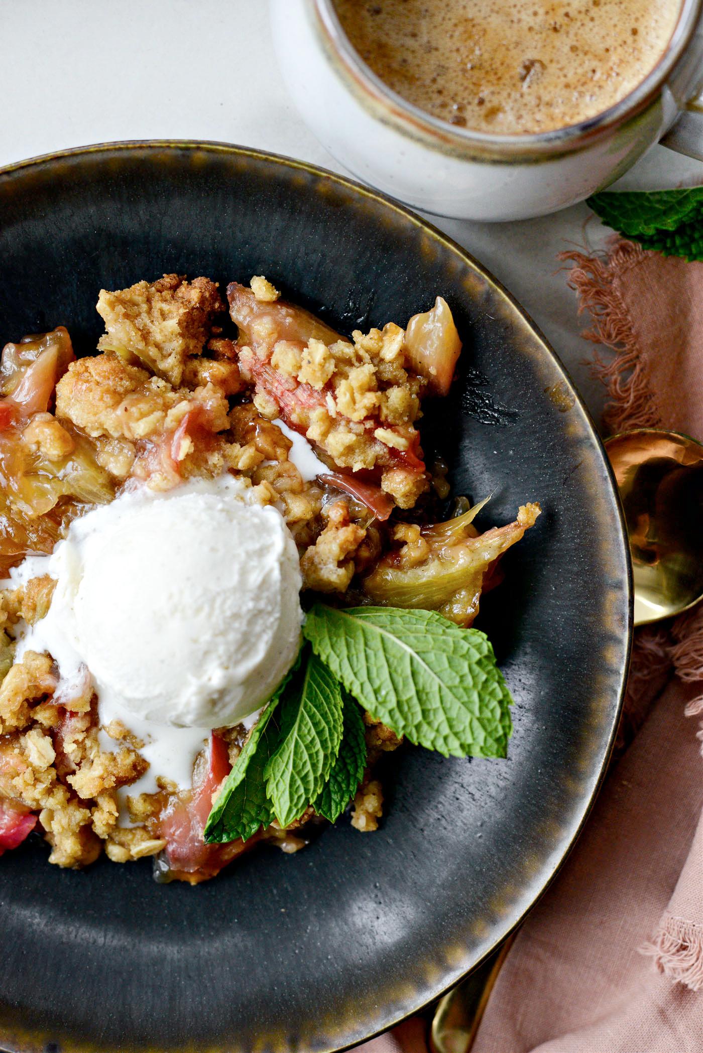 A rustic rhubarb and lemon crumble in a baking dish, with a scoop of vanilla ice cream on top