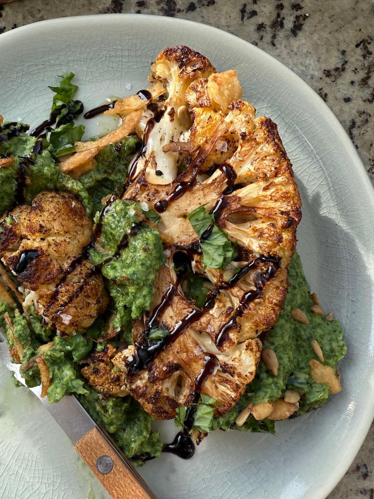 A beautifully plated dish of cauliflower steaks, drizzled with mushroom reduction glaze, garnished with fresh herbs